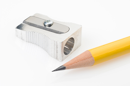 Close up of a yellow pencil tip and sharpener on white background. The pencil is on foreground with a sharp tip and the shiny metal pencil sharpener is on background.