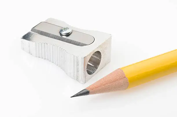 Close up of a yellow pencil tip and sharpener on white background. The pencil is on foreground with a sharp tip and the shiny metal pencil sharpener is on background.