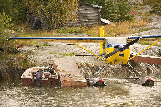 Seaplane or Float plane at an Arctic Camp. A seaplane, or floatplane sits at a wharf with a speed boat.  It is heavy rain and behind is a log camp or cabin. great slave lake stock pictures, royalty-free photos & images