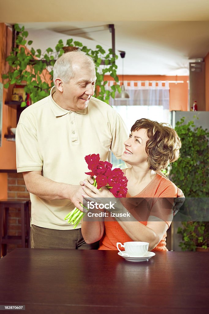 Uomo anziano offrendo fiori a sua moglie - Foto stock royalty-free di 55-59 anni