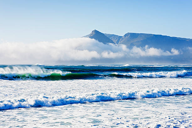 Dramatic sunlit seascape with surf, sea, clouds and mountain backdrop Vista across surf and sea to clouds and distant mountain. Shot with Canon EOS 1Ds Mark III. kommetjie stock pictures, royalty-free photos & images