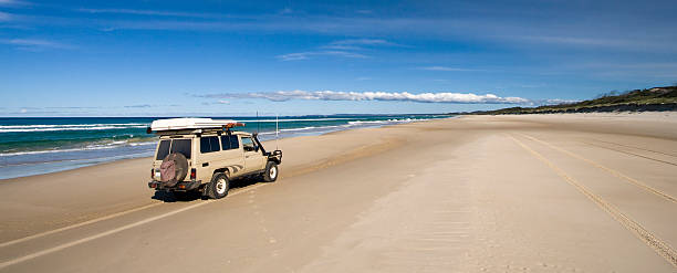 Vehicle driving along a smooth empty beach near the ocean An off-road vehicle cruising down the beach of Fraser Island's eastern coast. fraser island stock pictures, royalty-free photos & images