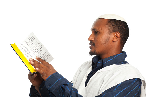 Ethiopian Jew wearing Talit and Kippa, reading Torah (Jewish Bible) isolated on white.