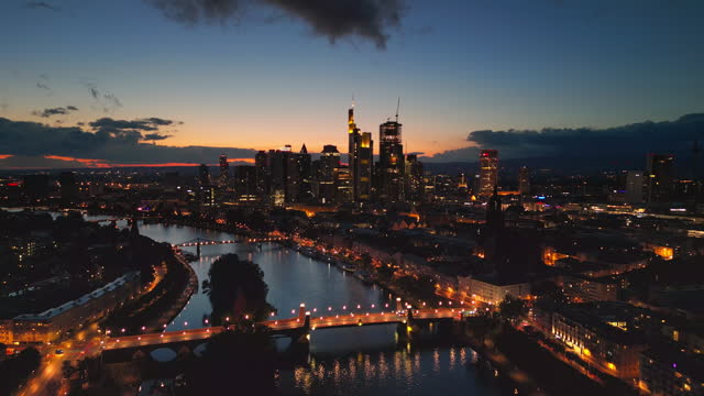 Aerial view Real time Footage of Frankfurt am Main skyline, though Main river and modern finance building and skyscrapers with Frankfurt Cathedral at sunset time, Germany