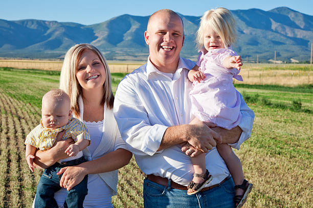 Rural Family Portrait Portrait of a young family of four standing in a fresh-cut hay field. mormonism stock pictures, royalty-free photos & images