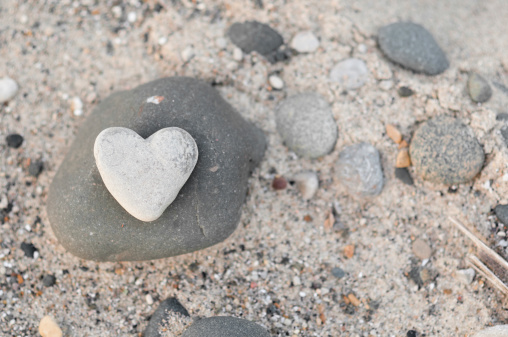 Color photo of a heart-shaped stone sitting amongst other rocks on the beach.