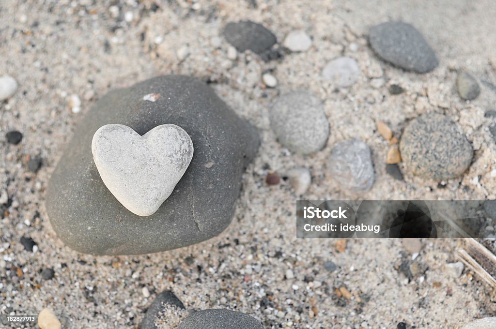 Heart-Shaped Stone with Other Rocks on Beach Sand Color photo of a heart-shaped stone sitting amongst other rocks on the beach. Heart Shape Stock Photo