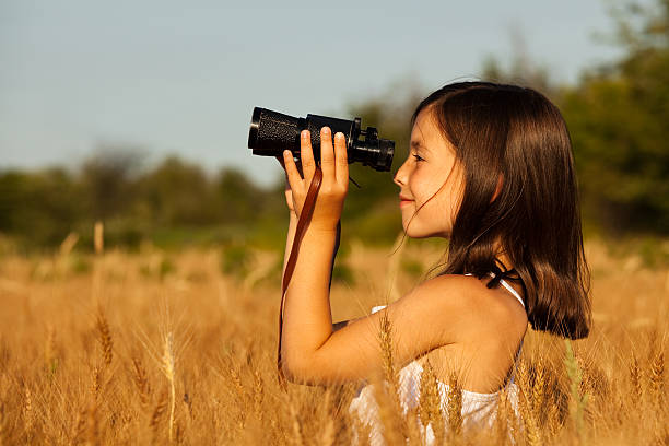 istock Cute young brunette with binoculars in field of brown-stalked grain. 182879974
