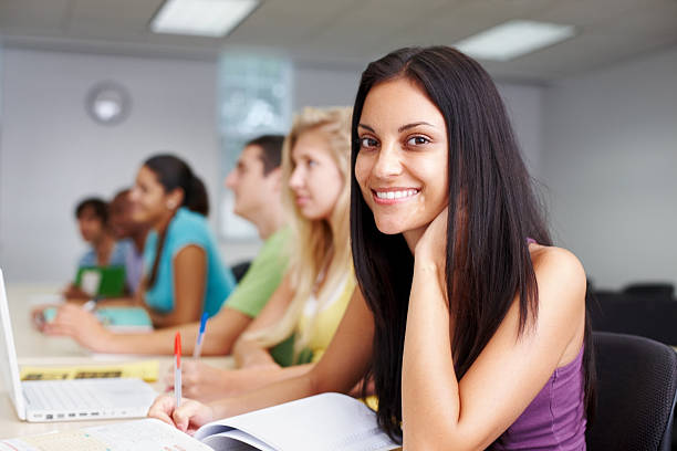istock Woman at desk writing notes with other students 182880080