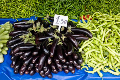 Eggplant and a variety of green peppers at an open fruit and vegetable market