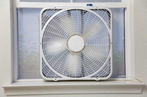 An operating box window fan in a window; blades are motion blurred.