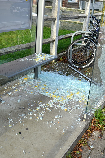 Leuven, Flemish-Brabant, Belgium - December 02, 2023: commuters their bicycles stand next to broken safety glass on a bench and ground of a glass wall of a bus stop in close-up