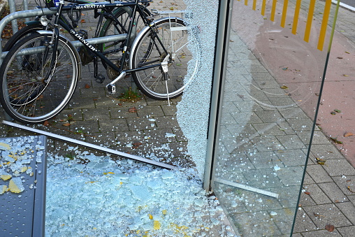 Leuven, Flemish-Brabant, Belgium - December 02, 2023: commuters their bicycles stand next to broken safety glass of a glass wall of a bus stop in close-up