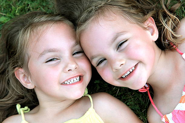 A close up portrait of 4 year old identical twin girls smiling at the camera.