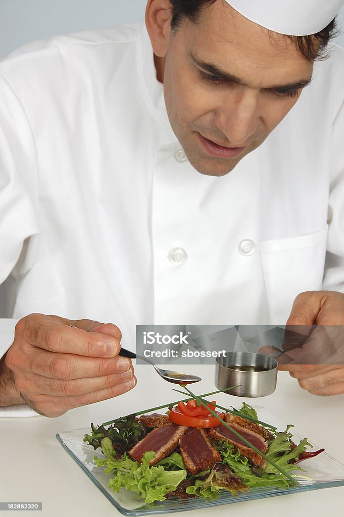 Chef Garnishing Seared Tuna Salad A restaurant chef putting the finishing touches on a salad of mesclun greens topped with rare seared ahi tuna. Pouring Stock Photo