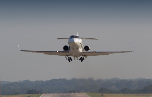 Head on perspective of a mid-sized business jet lifting from the runway in early morning light. Wheels are retracting emphasizing the departure. Horizontal perspective.
