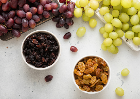 Sweet dried green and red dark raisins with ripe raw grapes on light background.Top view.