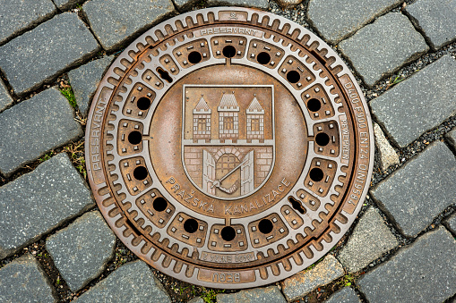 Prague, Czechia - September 18, 2022:  Manhole sewer cover on the cobblestone sidewalk stone brick of the streets of Prague Czech Republic Czechia