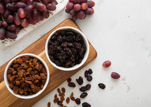 Two bowls with dried raisins with ripe red grapes on light background.