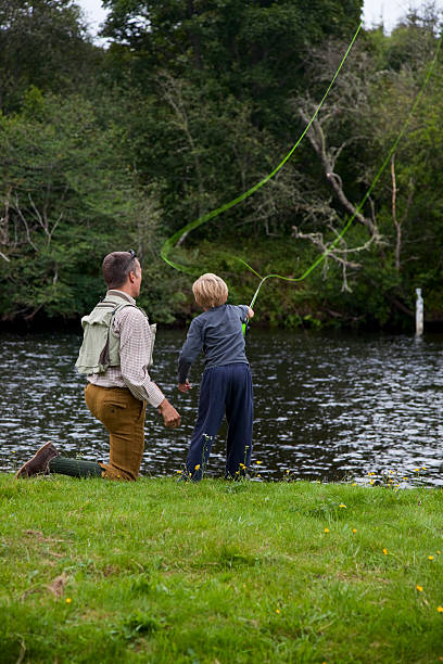 Son learning to fish with dad on the river Young son learning to cast using a fly fishing rod with his father. Movement blur on line. Fishing on the river Beauly in Scotland on holiday. fly fishing scotland stock pictures, royalty-free photos & images