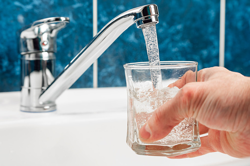 Hand holding a glass of water poured from a water tap.