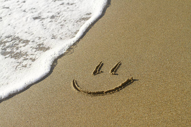 Smiley face on a beach next to a wave stock photo