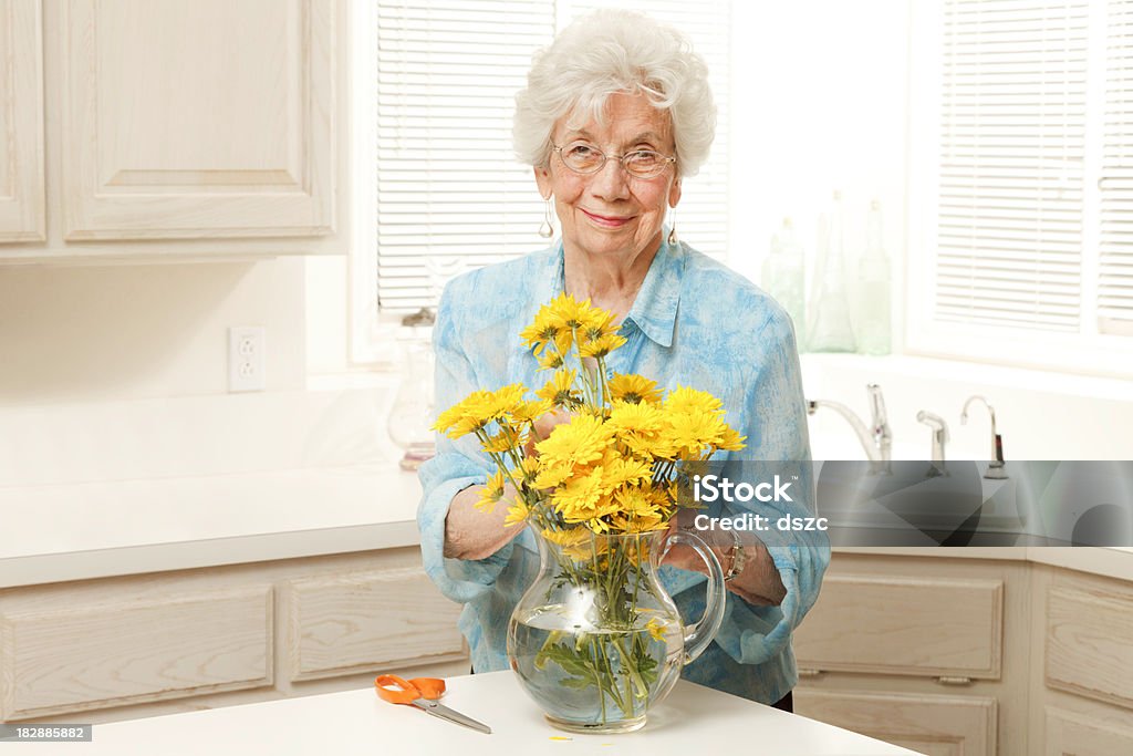 senior woman arranging cut yellow flowers in vase senior woman arranging cut yellow flowers in vase.Check out our other senior shots! 80-89 Years Stock Photo