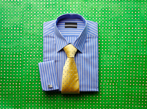 Blue striped shirt with yellow dotted tie and cufflinks on a green patterned background with copy space