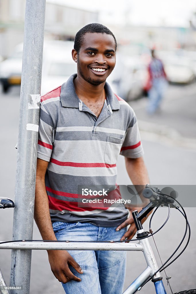 Smiling African man in street with bicycle "Handsome and happy young black man leans on a street pole, next to his bicycle. Shot with Canon EOS 1Ds Mark III." 20-29 Years Stock Photo