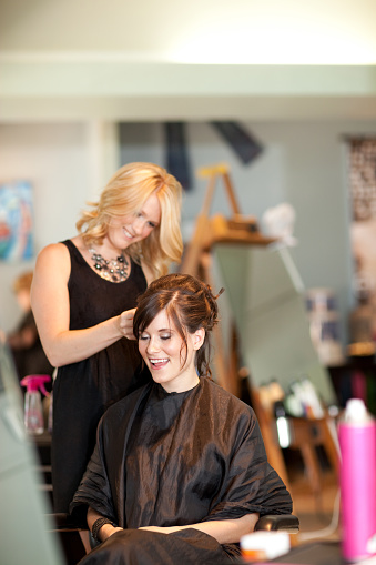 Color photo of a young woman getting her hair styled into an elegant updo in a salon.