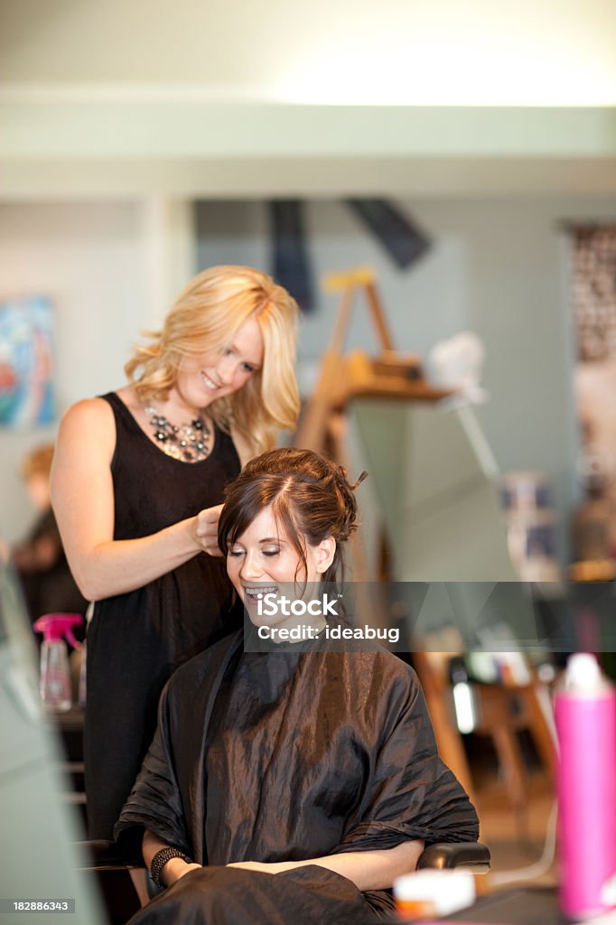 Young Woman Getting Hair Styled as Updo in Salon Color photo of a young woman getting her hair styled into an elegant updo in a salon. Hair Salon Stock Photo