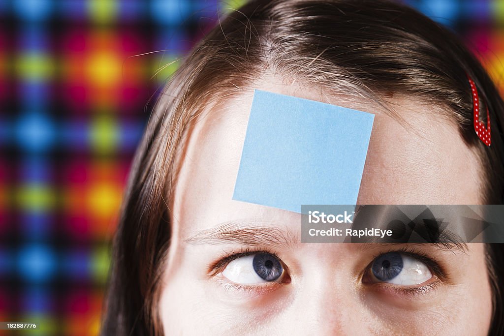 Payasear girl squints en blanco nota adhesiva en la frente - Foto de stock de 20 a 29 años libre de derechos