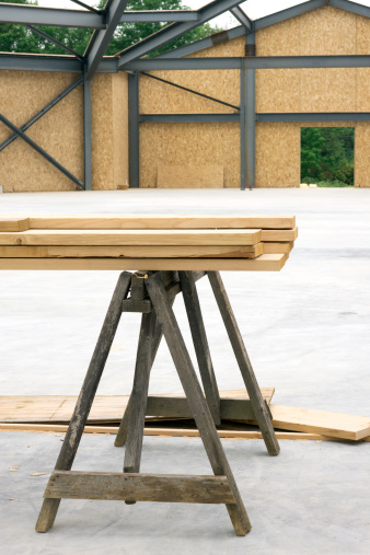 A stack of wood on a sawhorse sits in the middle of a newly cured cement floor at a construction site.Related image:
