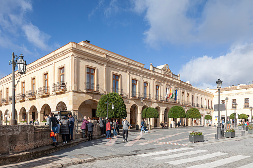 Ronda, Spain - 5th November 2023: Exterior of the Parador de Ronda, in the Plaza de España of the historic centre of the town of Ronda. Paradors are state-run luxury hotels, located in historic buildings. The Ronda Parador dates from 1761, and was previously the Town Hall. People are walking in the square and looking over the top of the Puente Nuevo over the El Tajo gorge (not in photo) over 300' / 90m below.
