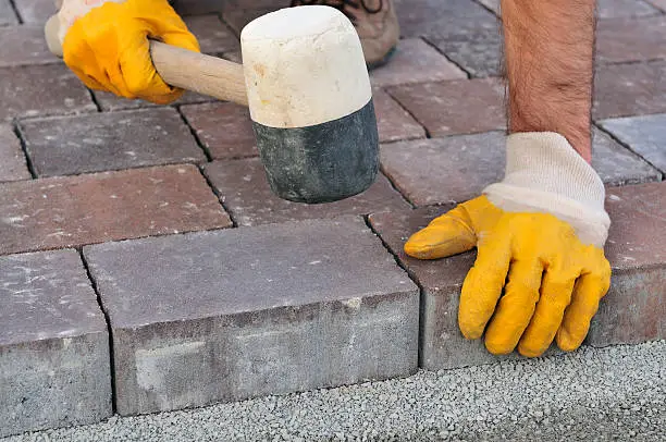 Mason is building pavement. Hands in yellow gloves lays layers of bricks.