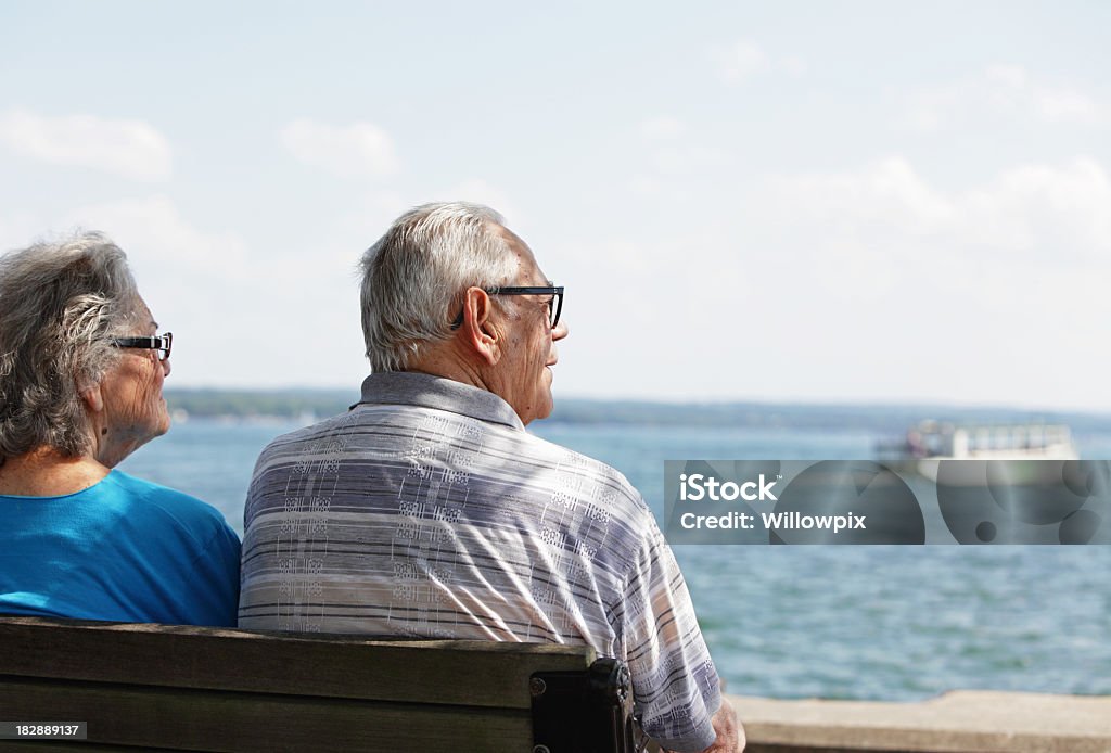 Casal sênior mulher no banco à sombra do Homem assistindo Lago barcos - Foto de stock de Adulto royalty-free