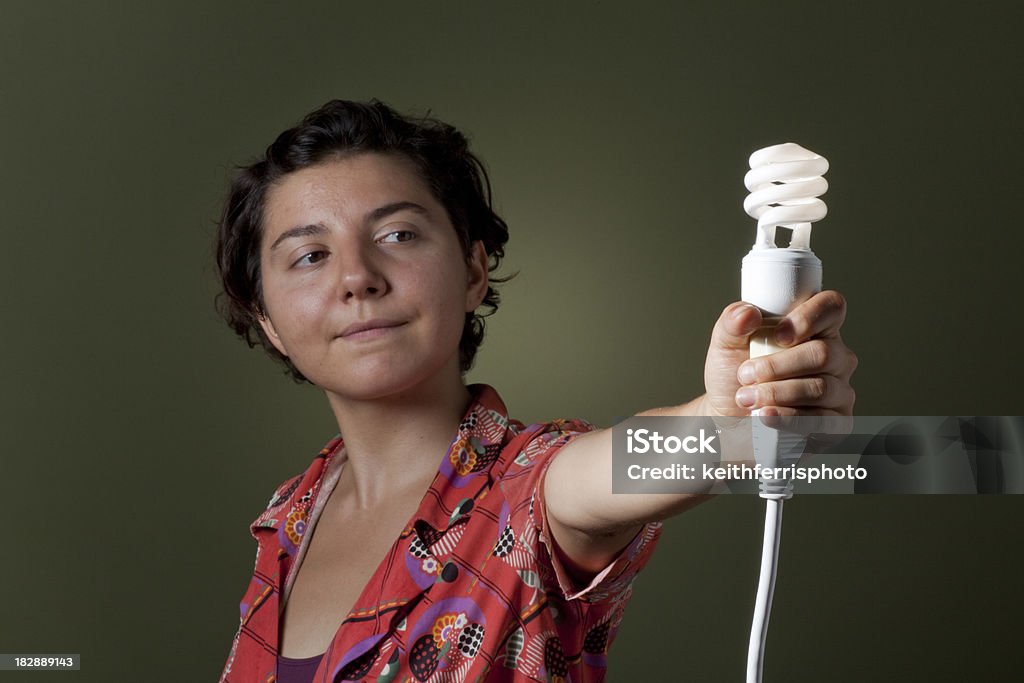 energy conservation concept A young woman holds an energy conserving CFL florescent lightbulb plugged into a power cord on a green background. You've got the power to change. Abstract Stock Photo