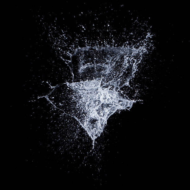 Splash of water in mid air against black background Picture of water exploding on a black backdrop.     spray stock pictures, royalty-free photos & images
