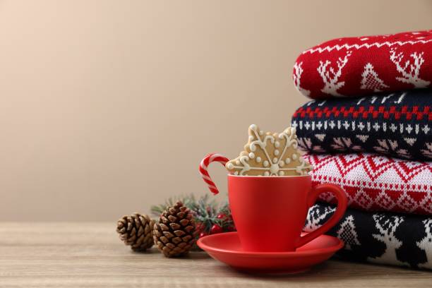 istock Stack of different Christmas sweaters, cup with candy cane, cookie and festive decor on wooden table, space for text 1828897449