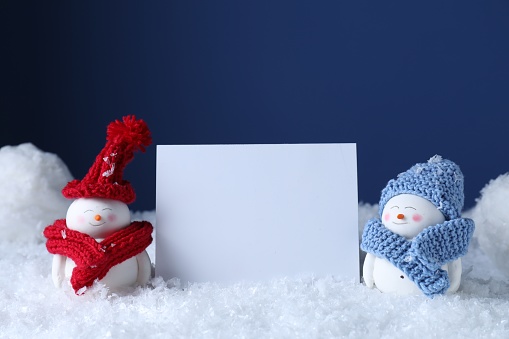 Cute decorative snowmen and blank card on snow against blue background
