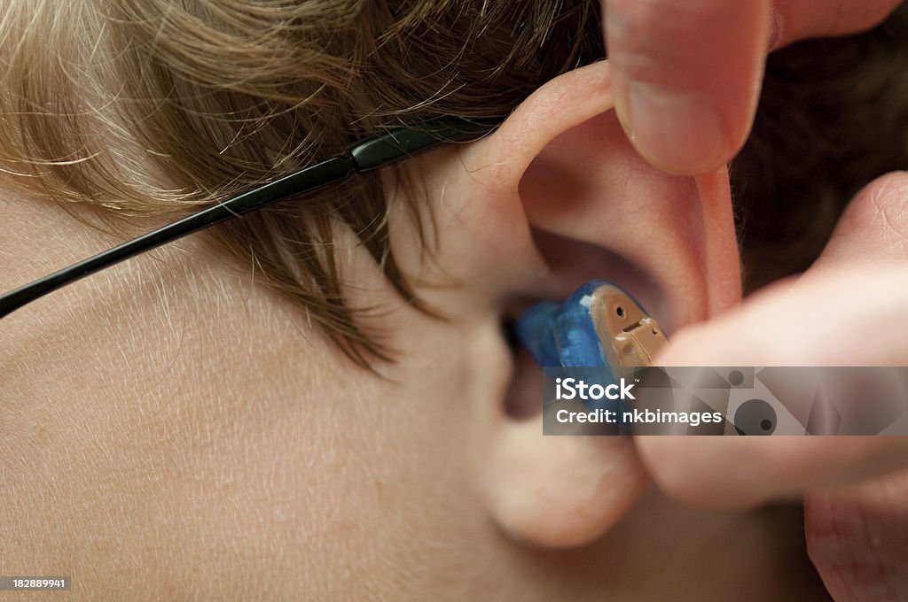 Inserting completely in the canal (CIC) hearing aid child's ear Horizontal image of a completely in the canal (CIC) hearing aid being inserted into a child's ear.  Left hearing aids are typically blue and right are red.  Focus is on the top of the hearing aid faceplate with a shallow depth of field.  More hearing aids: Hearing Aid Stock Photo