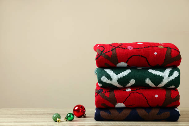 istock Stack of different Christmas sweaters and baubles on wooden table against beige background, space for text 1828900223