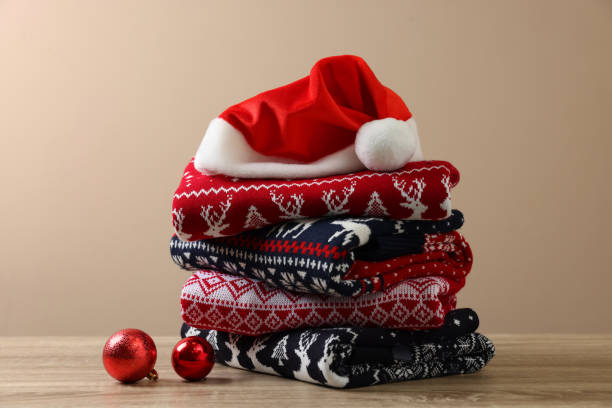 istock Stack of different Christmas sweaters, Santa hat and baubles on wooden table against beige background 1828900279