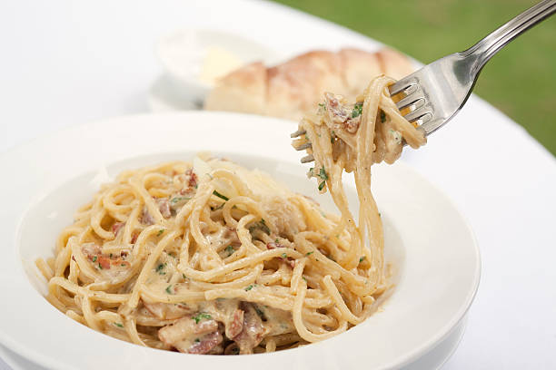 A fork spindles from a bowl of linguine carbonara 