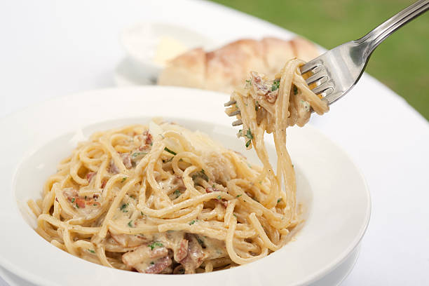 A fork spindles from a bowl of linguine carbonara  stock photo