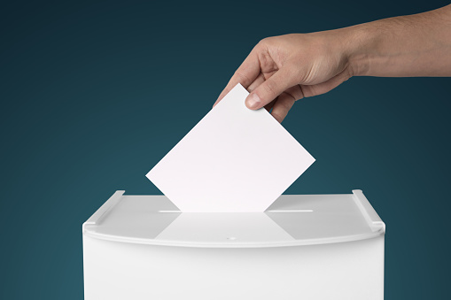 Man putting his vote into ballot box on gradient color background, closeup