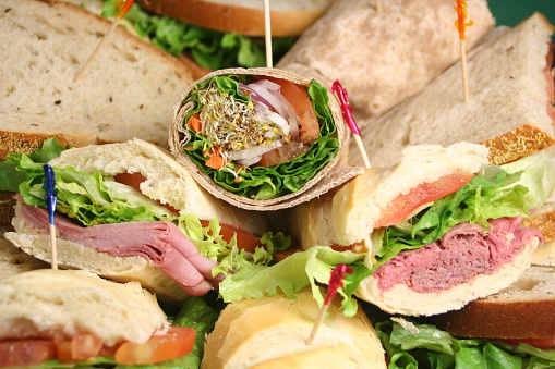 Beautifully decorated catering banquet table with different food snacks and appetizers setting with sandwiches, bagels, baguette club submarine sandwich, on a wooden plate, party or celebration