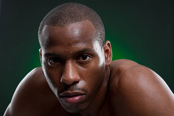 An African American boxer looking directly into the camera with sweat dripping from his brow after a strenous workout getting ready for his next fight.