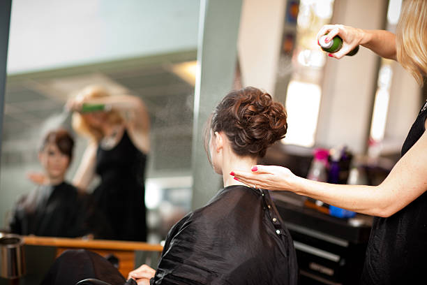 Young Woman Getting Hair Styled as Updo in Salon Color photo of a young woman getting her hair styled into an elegant updo in a salon. salon mirror stock pictures, royalty-free photos & images