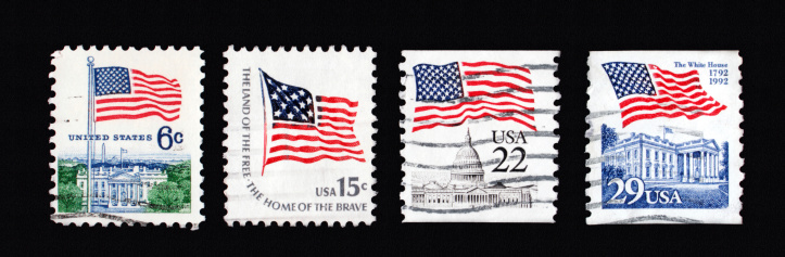 Four canceled first class stamps with United States of America flags of different value on black backgroundMore images with stamps: